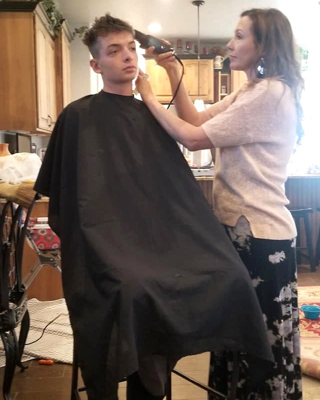Char cutting a client's hair at a stool in his kitchen.